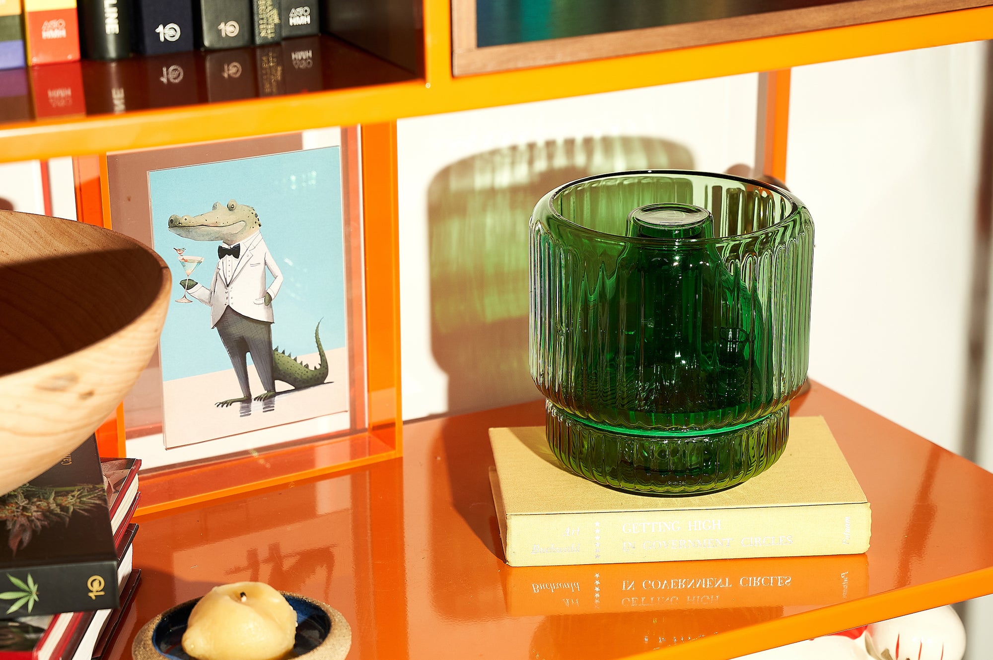 A green ribbed glass vase bong styled discreetly on a modern orange bookshelf, sitting atop a book titled Getting High in Government Circles. A clever and decorative bud vase alternative that blends into playful home decor with a mid-century vibe.