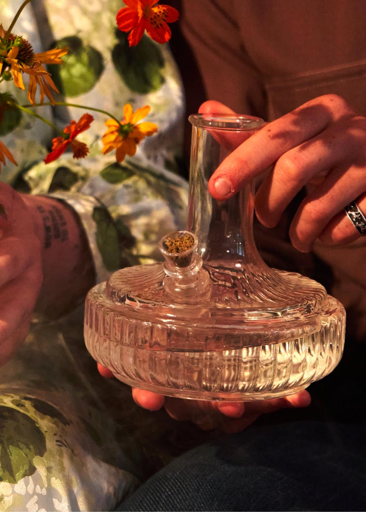 Person holding clear ribbed glass bong packed with flower on warm indoor set