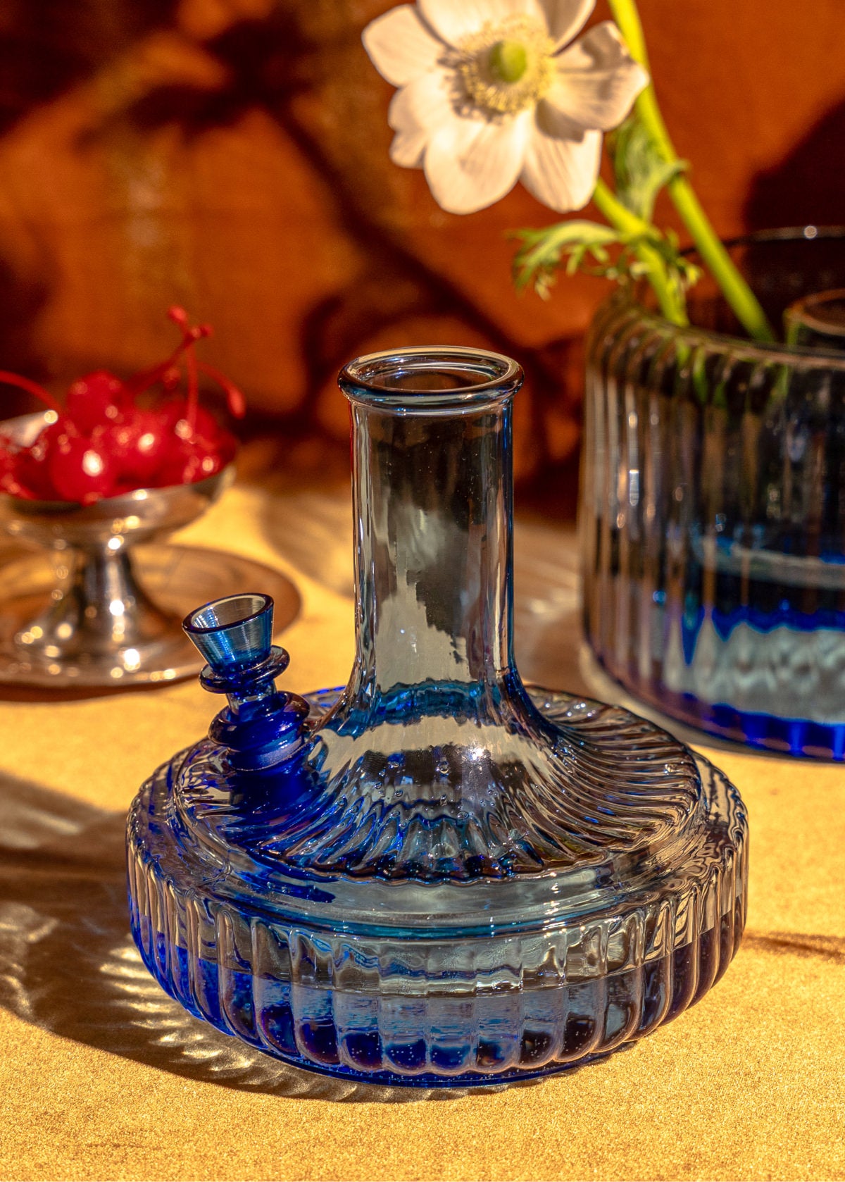 Blue decorative glass bong styled beside flowers and cherries on a table setting