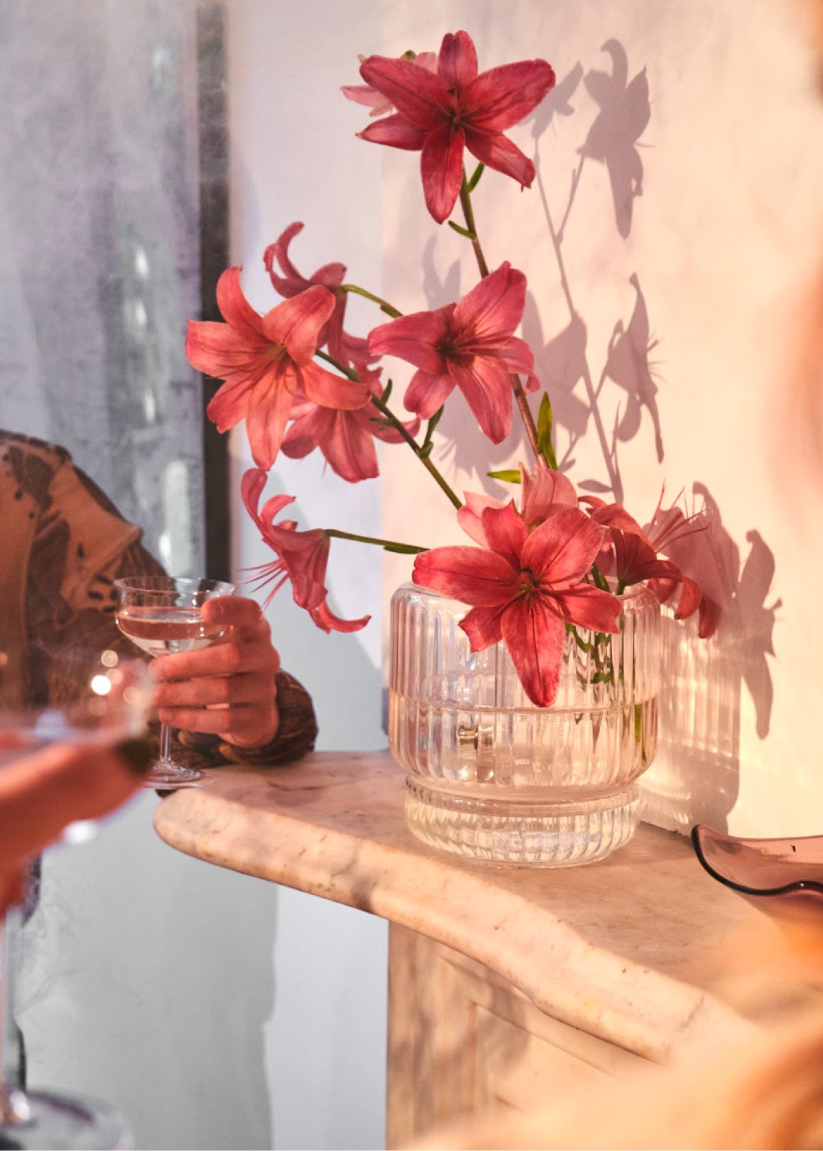 Clear ribbed flower vase with pink lilies styled on marble mantel during gathering